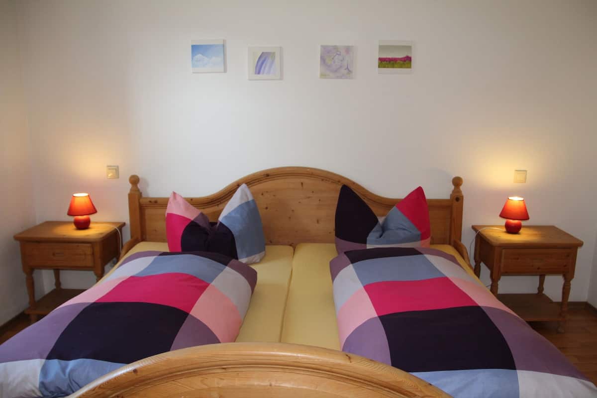 Ein Doppelbett mit Holz-Kopfteil, zwei Nachttische mit Lampen und eine farbenfrohe Steppdecke.