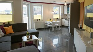 A modern living room with a sofa, a dining table, and a kitchen area.