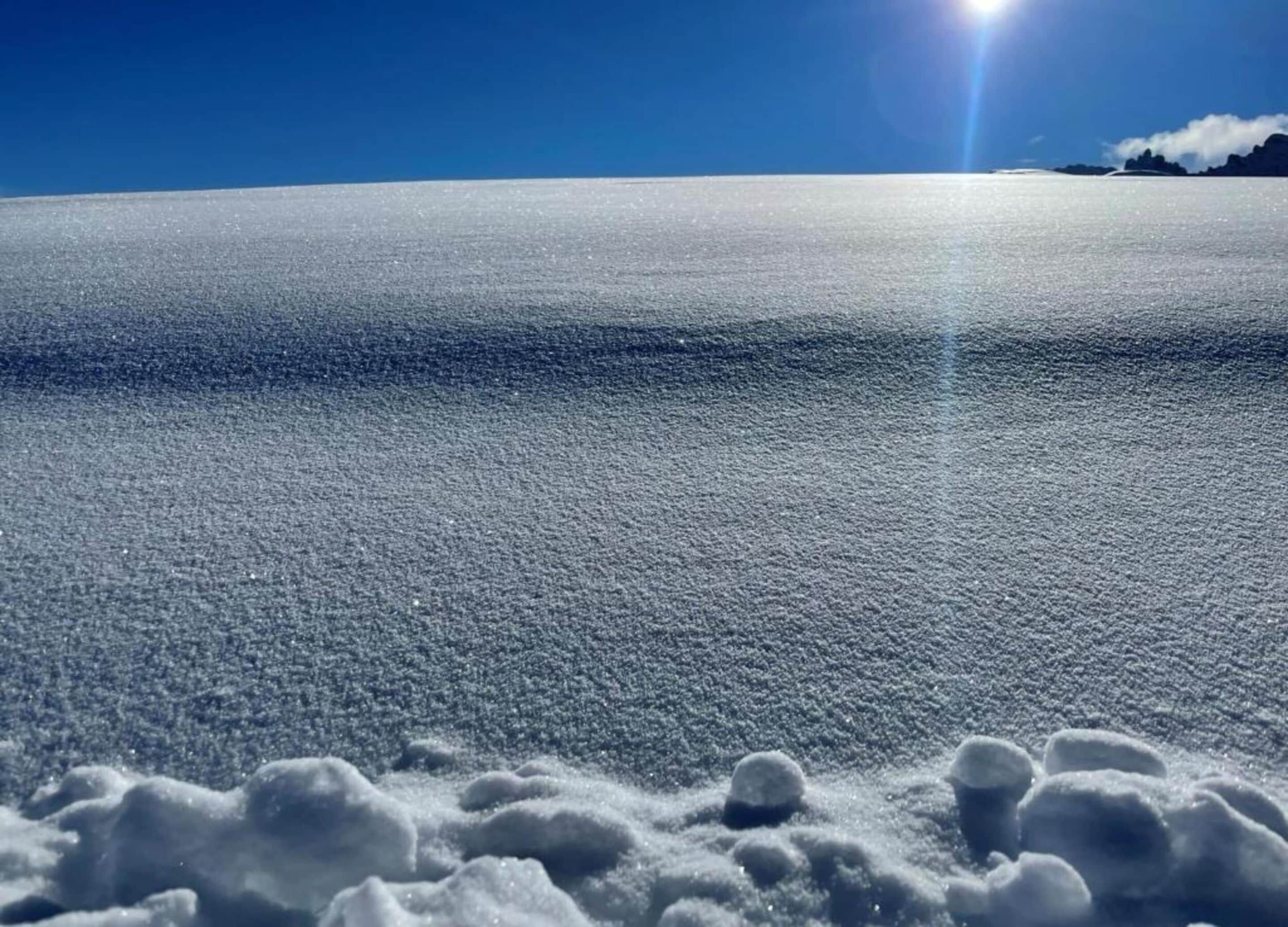 A vast, flat, icy landscape under a clear blue sky with the sun shining directly overhead.