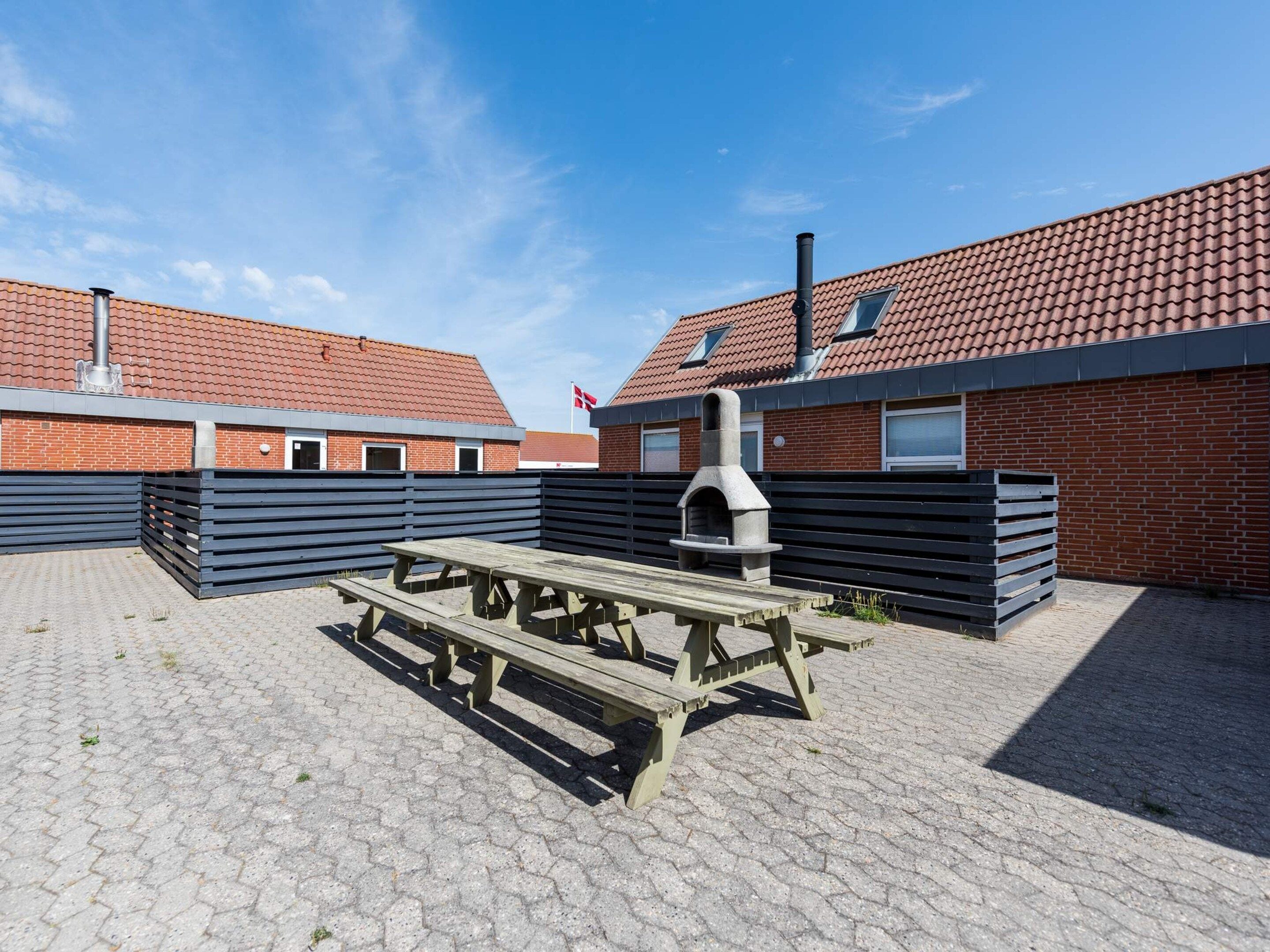 A courtyard with a barbecue grill, picnic tables, and a brick building with a tiled roof.