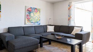 Ein modernes Wohnzimmer mit einem grauen Ecksofa, einem schwarzen Couchtisch und einem farbenfrohen, abstrakten Gemälde an der Wand.