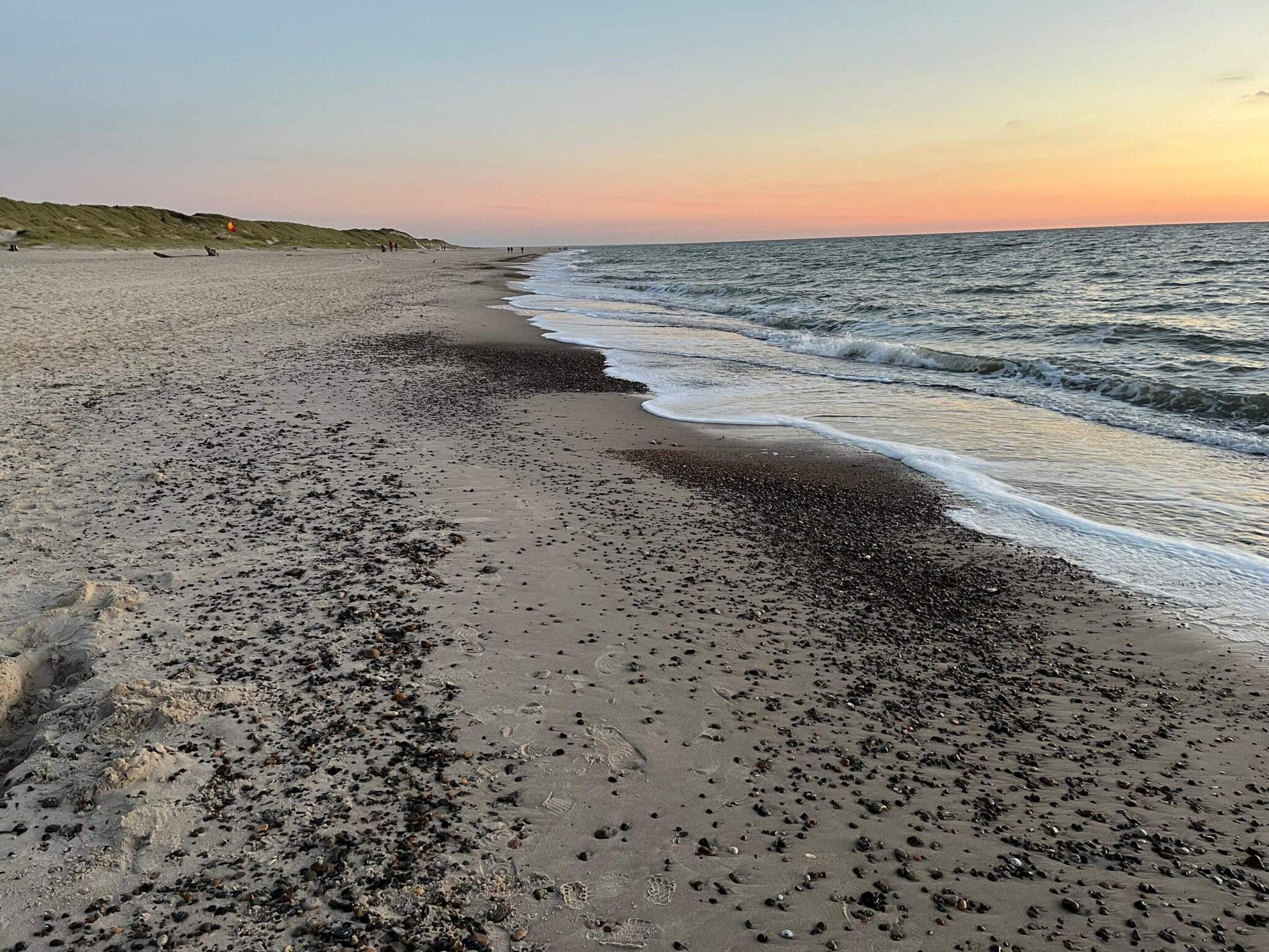 A beach with pebbles and sand, a gentle sea, and a sunset.