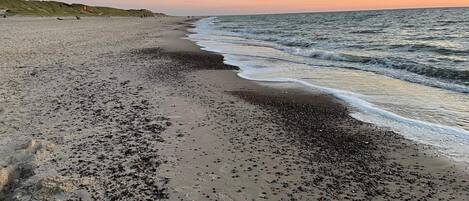 A beach with pebbles and sand, a gentle sea, and a sunset.