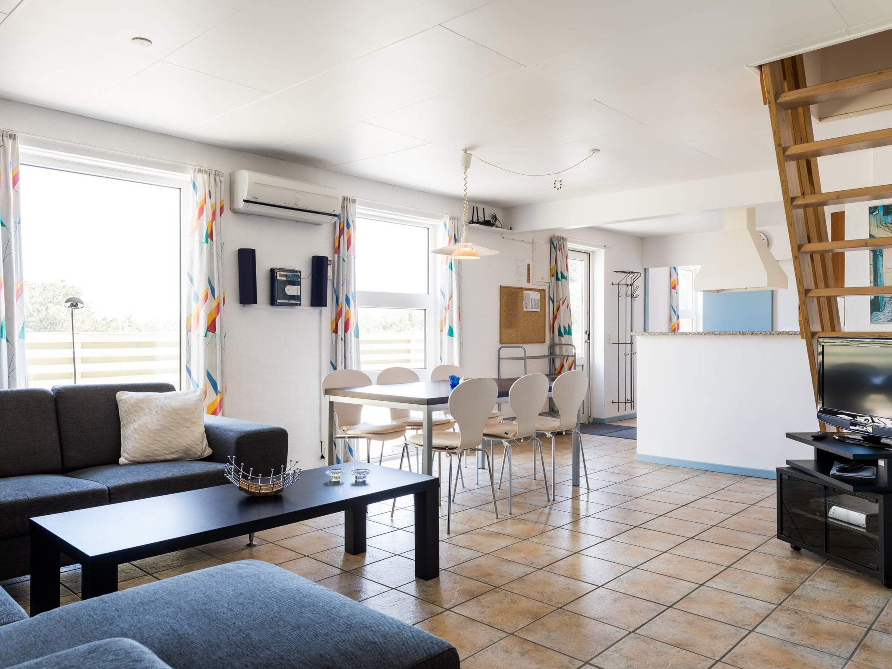 Een moderne woonkamer met een bank, een eettafel met stoelen, een televisie en een trap.