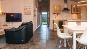 Ein modernes Interieur mit einer Ledersofa, einem Esstisch mit Stühlen, einer Küchenzeile und einem an der Wand montierten Fernseher.