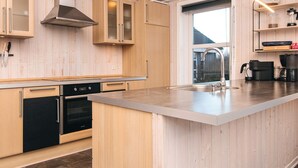 Eine moderne Küche mit Holzschränken, einer Edelstahl-Dunstabzugshaube, einem eingebauten Ofen und einer großen Kochinsel mit Spüle.
