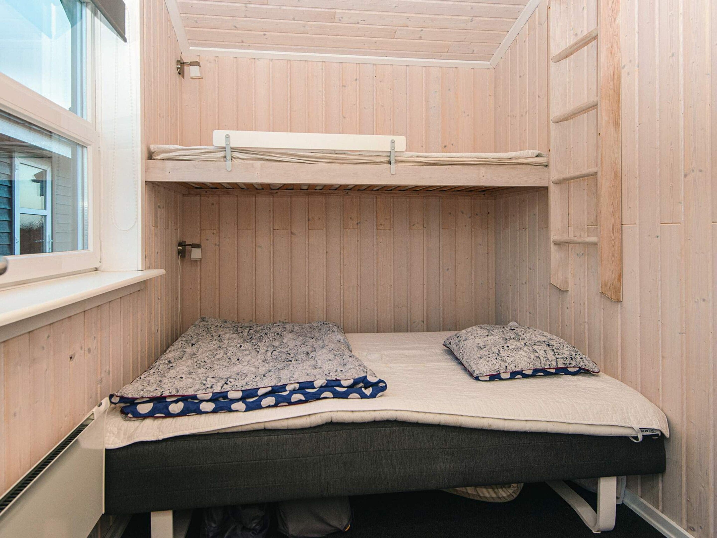 A small, wooden-paneled room with a bunk bed, two pillows, and a window.