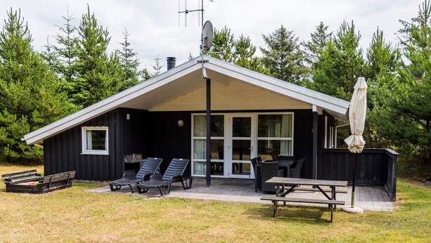 Eine kleine Holzhütte mit einer überdachten Veranda, Sitzgelegenheiten im Freien und einer Satellitenschüssel.