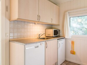 A kitchen with white cabinets, a microwave, a dishwasher, and a window with a view of trees. - 4 Star Holiday Home in Henne (Henne)