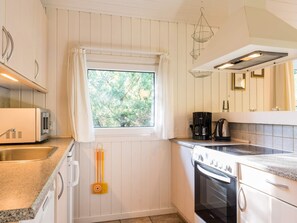 A kitchen with white cabinetry, a window with a view of trees, a coffee maker, and a stove.