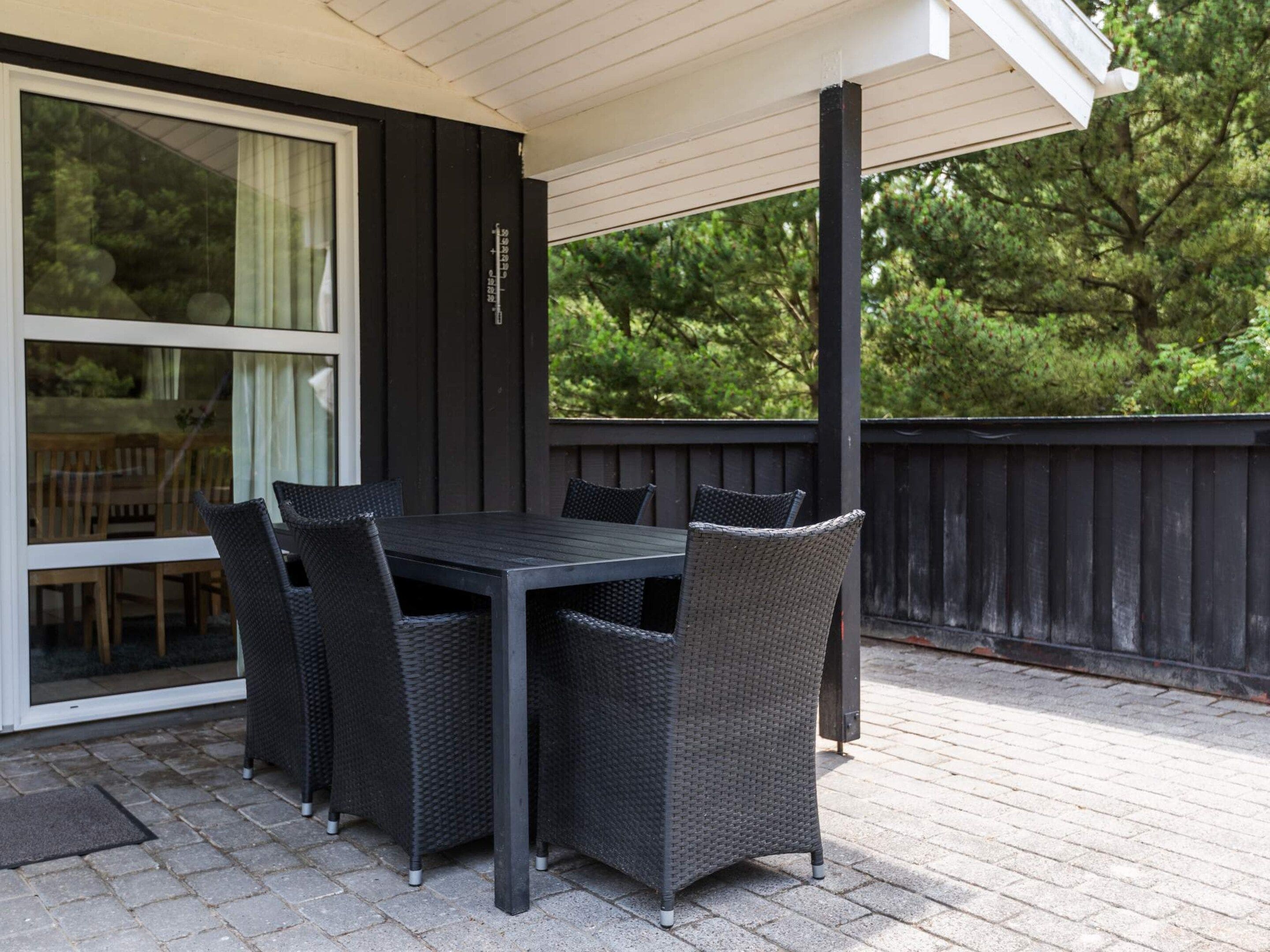 An outdoor patio with a table and chairs, a wooden deck, and a view of trees.
