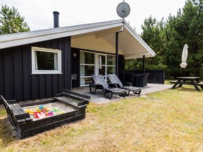 A black building with a covered patio area, outdoor seating, and a sandbox. - 4 Star Holiday Home in Henne (Henne)