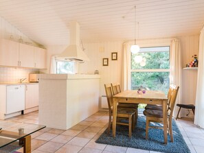 A modern kitchen with white cabinetry, a central island, and a dining area with a table and chairs. - 4 Star Holiday Home in Henne (Henne)