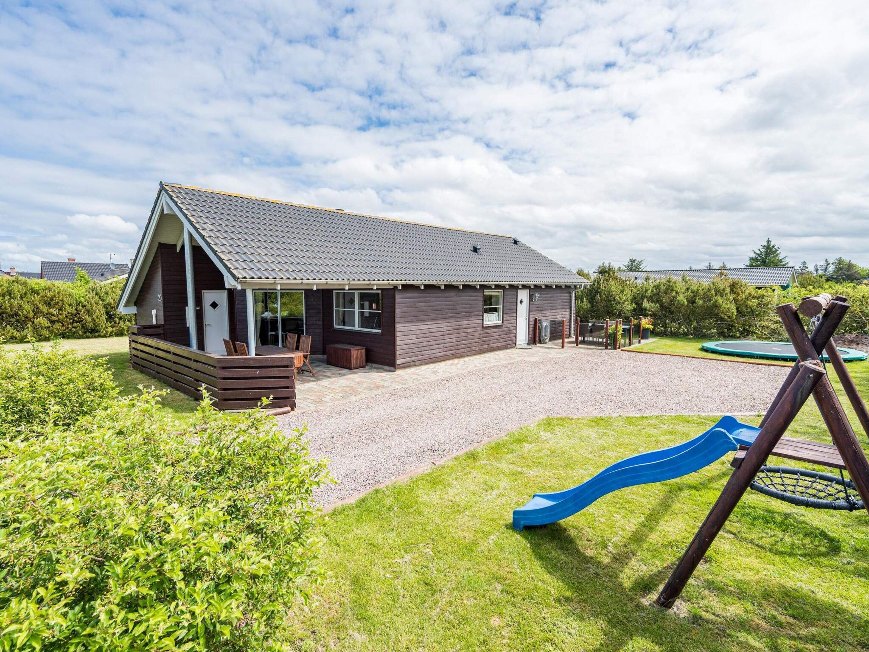 A two-story house with a covered patio, a gravel driveway, and a playground with a slide.