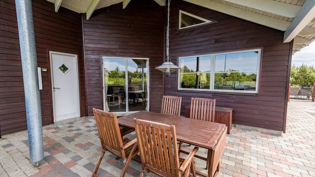 A patio with a wooden table and chairs, a sliding glass door, and a view of the outdoors. - 4 Star Holiday Home in Tarm (Tarm)