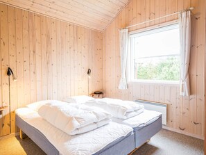 Habitació amb parets de fusta, un llit amb roba de llit blanca, una taula de nit, una finestra amb cortines i una làmpada penjada a la paret.