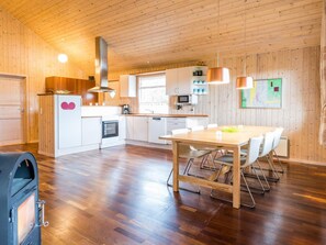 A modern kitchen with wooden walls, a dining area with a table and chairs, and a built-in oven.