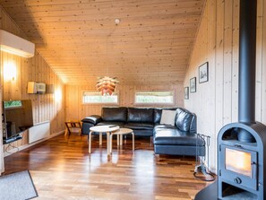 A cozy cabin interior with a wooden ceiling, a black leather sofa, a small table, a fireplace, and a television.