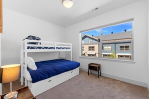 A bunk bed with a blue mattress, a bedside table with a lamp, and a window with a view of neighboring houses. - The Highland Hangout: Luxurious, new 3 bed, 3 bath townhome in McCall with garage (McCall)