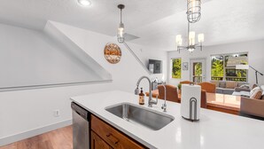 Una cocina moderna con lavavajillas integrado, un lavabo y un armario de madera. Hay una zona de comedor con un sofá y una mesa de centro.