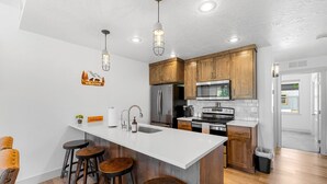 Una cocina moderna con armarios de madera, una isla grande con taburetes, electrodomésticos de acero inoxidable e iluminación colgante.