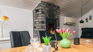 Un coin repas avec une table en bois, des chaises, un vase de tulipes, un plateau avec des verres et une cheminée.