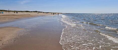 A beach with a wide sandy shore, gentle waves, and a clear sky.