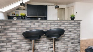 Une cuisine moderne avec un mur de fond en briques, deux tabourets de bar noirs et des luminaires suspendus.