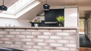 Une cuisine avec un mur recouvert de briques, un plan de travail noir, un réfrigérateur blanc et une lucarne au-dessus.