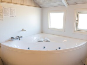A large, white bathtub with chrome fixtures, a wooden ceiling, and two small windows.