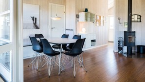 A modern kitchen with wooden paneling, a dining area with black chairs, and a wood-burning stove. - Bright Dune View Cottage-by Traum (Hvide Sande)