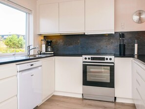 A modern kitchen with white cabinets, a dishwasher, an oven, and a coffee maker.