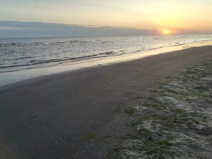 A beach with a sunset, waves, and a clear sky.