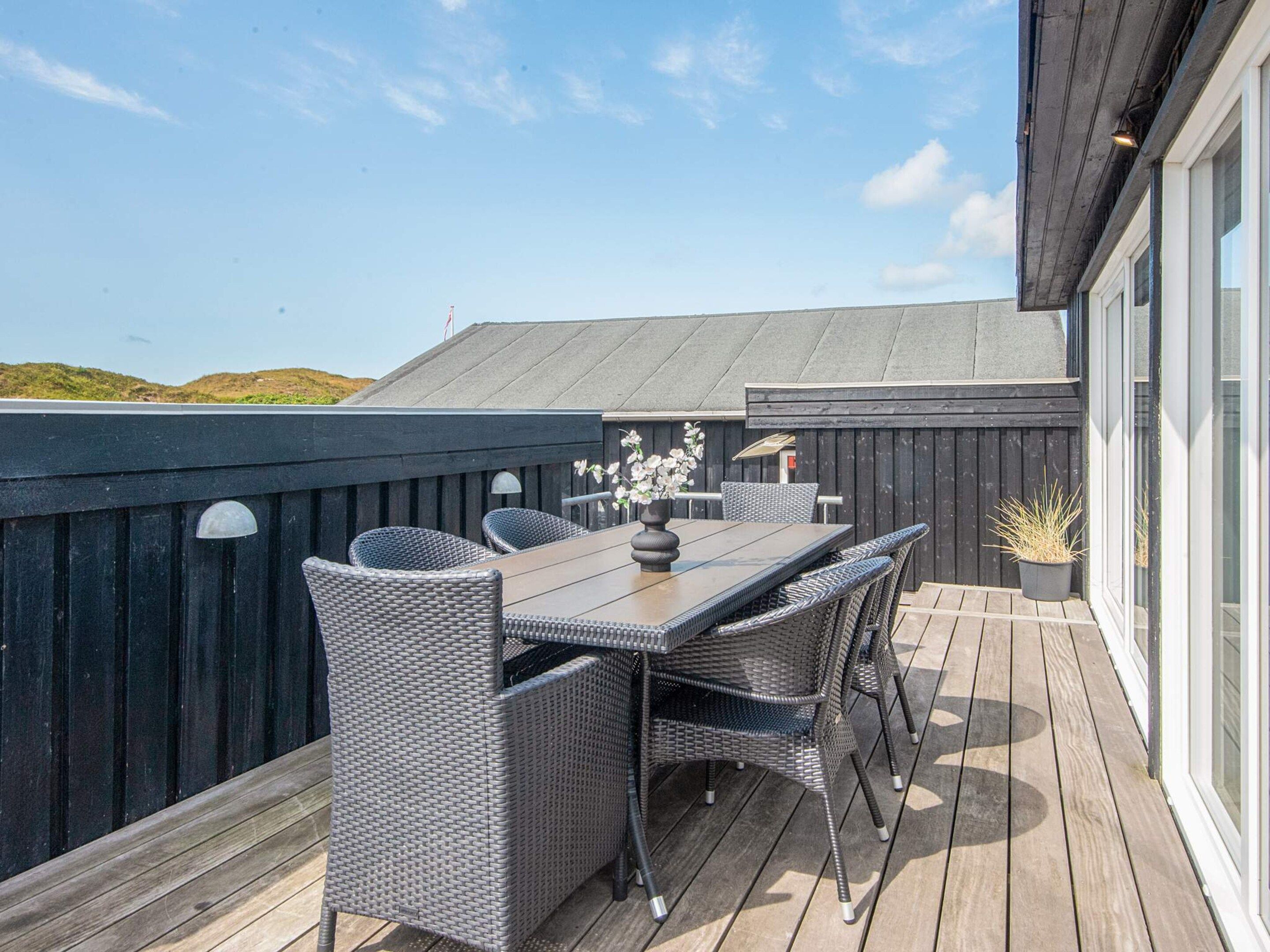 Een overdekt terras met een tafel, stoelen, een potplant en uitzicht op het landschap.