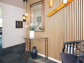 A room with a round glass table, a white vase with flowers, a black vase, a wooden wall with vertical slats, a mirror, and a clock.