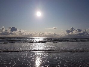 A beach with waves, a clear sky, and the sun.