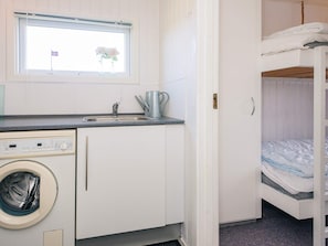 A compact kitchenette with a washing machine, a sink, and a window with flowers.