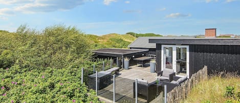 Eine moderne Außenterrasse mit Sitzgelegenheiten und einer Glastür zu einem überdachten Bereich.