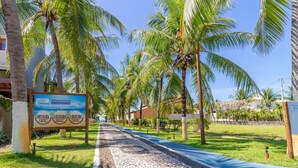 A paved pathway lined with palm trees and a signboard. - GB19 Casa 7 Quartos a 50m da Praia (Camaçari)