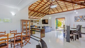 A spacious living area with a high ceiling, a dining table with chairs, a sofa, and a TV mounted on the wall. - GB19 Casa 7 Quartos a 50m da Praia (Camaçari)