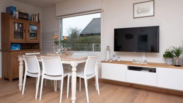 A modern kitchen with a dining table, chairs, a TV, and a window. - Quiet Home with Garden near Beach & Center (Renesse)
