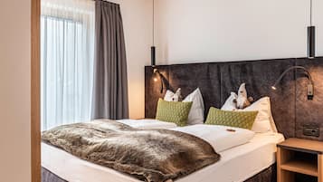 Ein Doppelbett mit brauner Decke, ein Kopfteil mit Wandleuchten und ein Nachttisch mit Lampe.