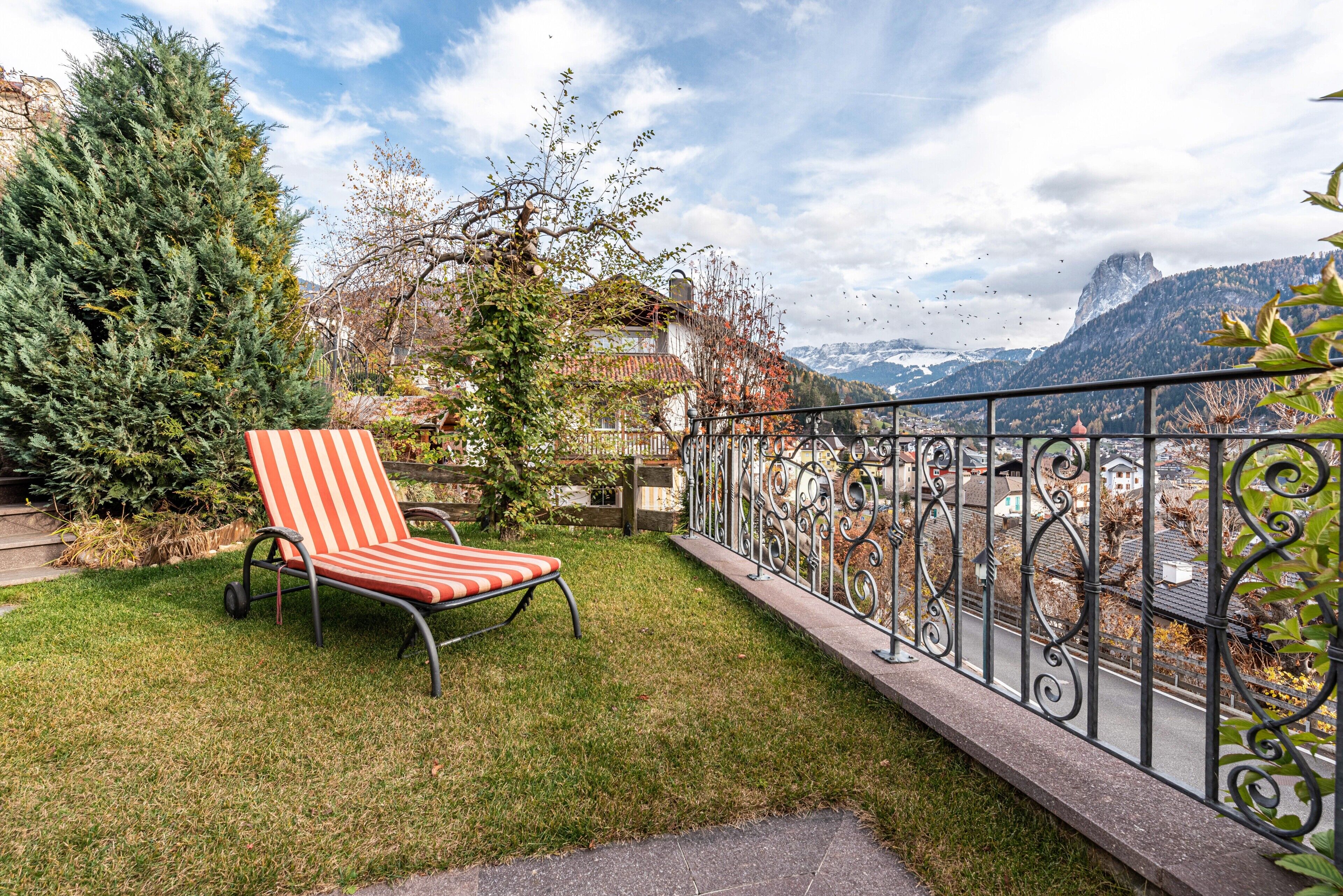 Ein Balkon mit einem gestreiften Stuhl, einem Metallgeländer und Blick auf einen Berg.