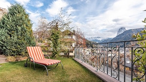 Un balcone con una sedia a righe, una ringhiera in metallo e vista su una montagna.
