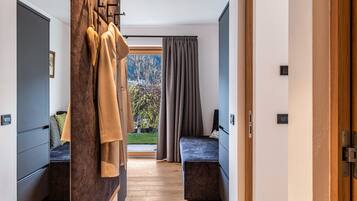 Ein modernes Hotelzimmer mit Holzboden, einem Bett mit dunklem Kopfteil, einer Sitzecke mit einer Bank und Blick auf Bäume durch ein Fenster.
