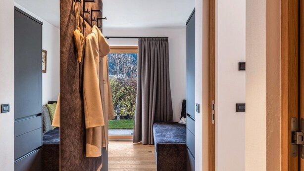 Una camera d'albergo moderna con pavimento in legno, un letto con testiera scura, una zona relax con una panca e vista su alberi attraverso una finestra.