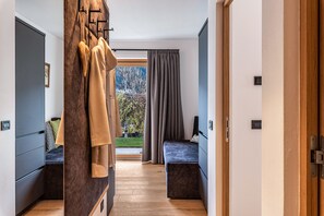Een moderne hotelkamer met een houten vloer, een bed met donker hoofdeinde, een zithoek met een bankje en uitzicht op bomen door een raam.
