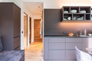 A modern kitchen with grey cabinets, a built-in shelf with dishes, and a wooden floor. - Apartment “Saslonch” near Seiser Alm with Mountain View, Wi-Fi, Terrace & Garden (St. Ulrich)
