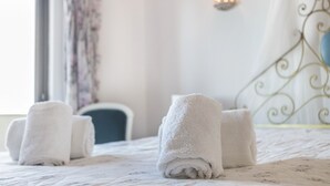 Een net opgemaakt bed met opgerolde witte handdoeken, een wandlamp en een decoratief metalen hoofdbord.