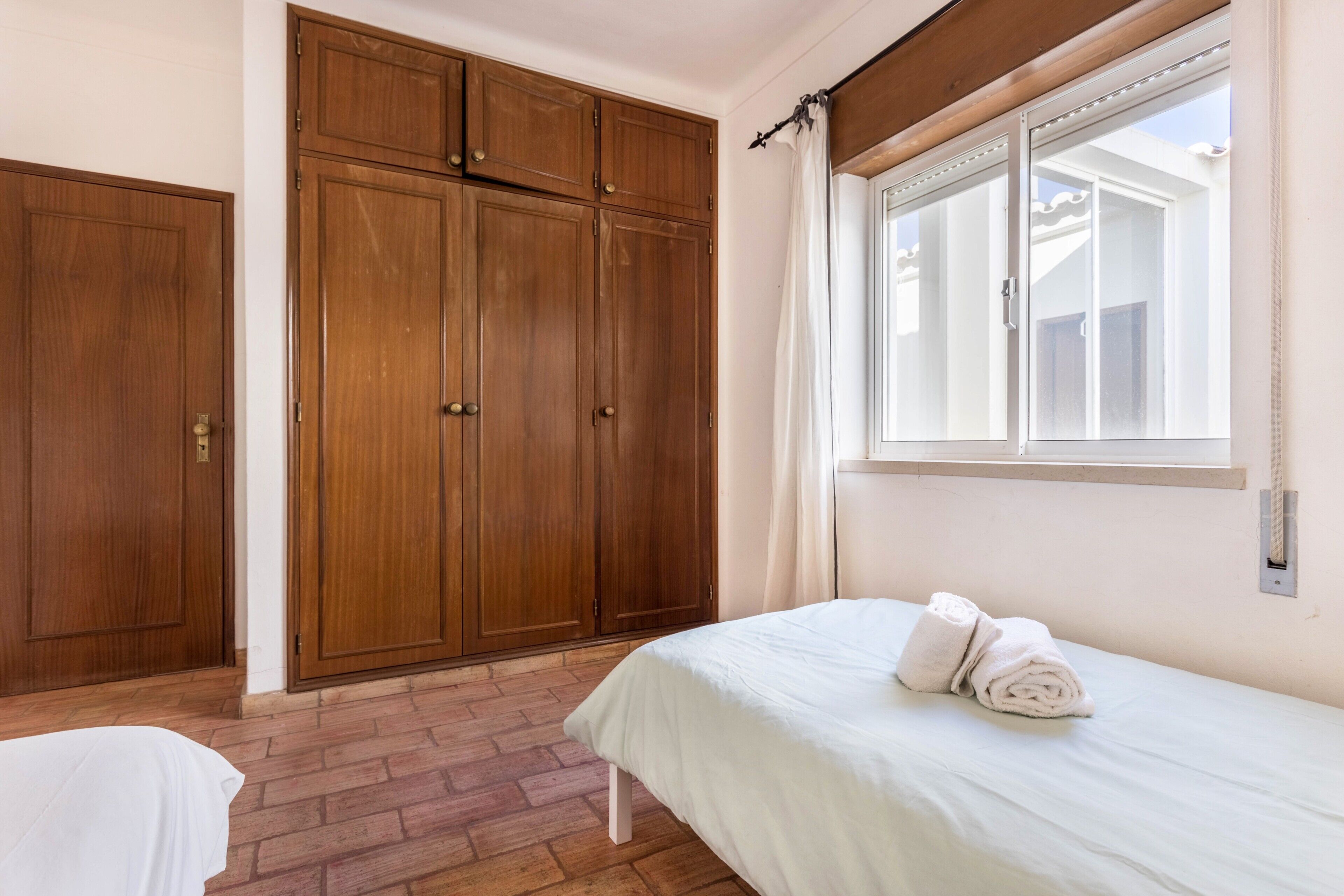 A bedroom with a bed, a wardrobe, and a window with curtains.